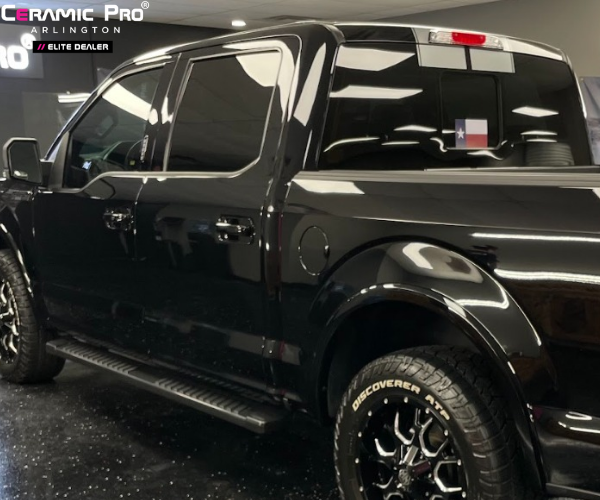 A front three-quarter view of a black SUV with dark tinted windows, parked in a professional detailing garage with a high-gloss reflective finish.