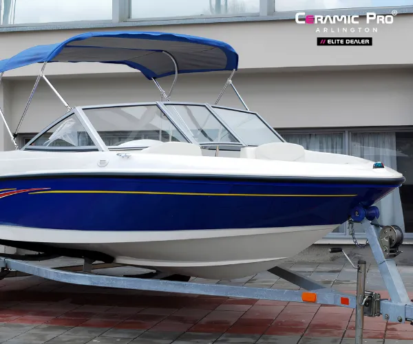 view of a clean, blue and white speed boat with a blue bimini top resting on a trailer, as seen in boat detailing